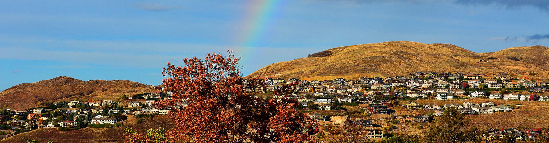 Foothills with houses on them and rainbow in background